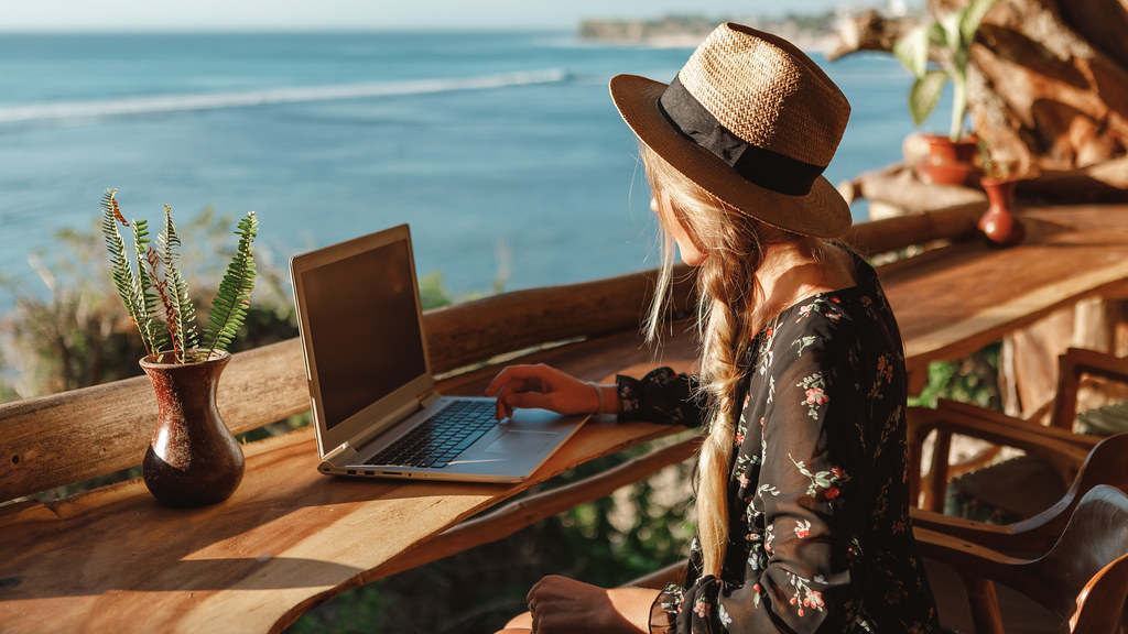 Woman working on laptop overlooking a beach - AdobeStock